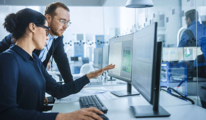 VD och produktionsledare i samtal framför en dator i en industriell miljö, i samverkan kring produktionsdata eller beslutsunderlag